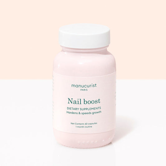 A pink bottle labeled Manucurist Nail Boost contains 60 nail supplement capsules for a 1-month routine, designed to strengthen and speed nail growth. Features a white cap and is set against a light pink and white background.