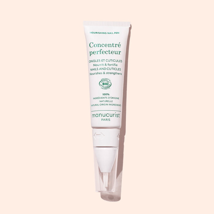 A white tube of Manucurist Nourishing Nail Pen - Cosmos Organic with green text stands upright against a light pink background—ideal for nail and cuticle care.
