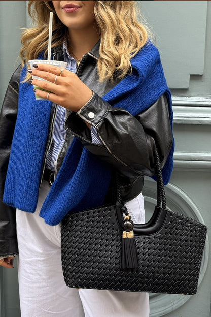 Person wearing a blue coat and black leather jacket, holding a black woven handbag.
