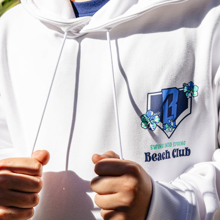 White hoodie with a floral BL101 logo and 'Swing into Spring Beach Club' text on the chest, held by a person.