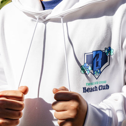 White hoodie with a floral BL101 logo and 'Swing into Spring Beach Club' text on the chest, held by a person.