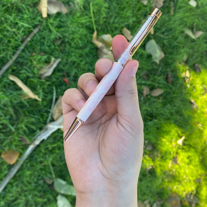 Hand holding a pink pen with gold accents against a grassy background