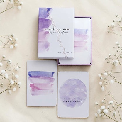 Purple and white card deck with 'practice you' packaging on a beige background with flowers.
