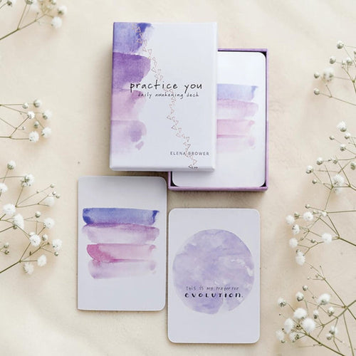 Purple and white card deck with 'practice you' packaging on a beige background with flowers.