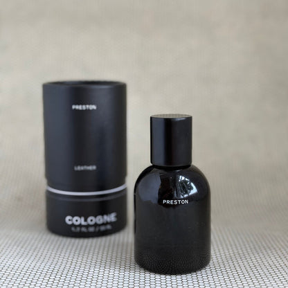 Black Preston leather cologne bottle and packaging on a textured surface with a neutral background