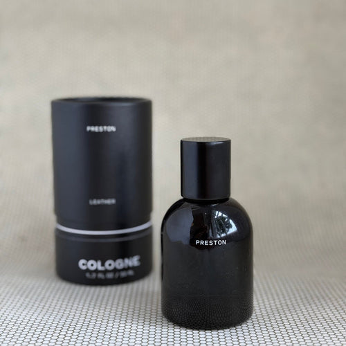 Black Preston leather cologne bottle and packaging on a textured surface with a neutral background