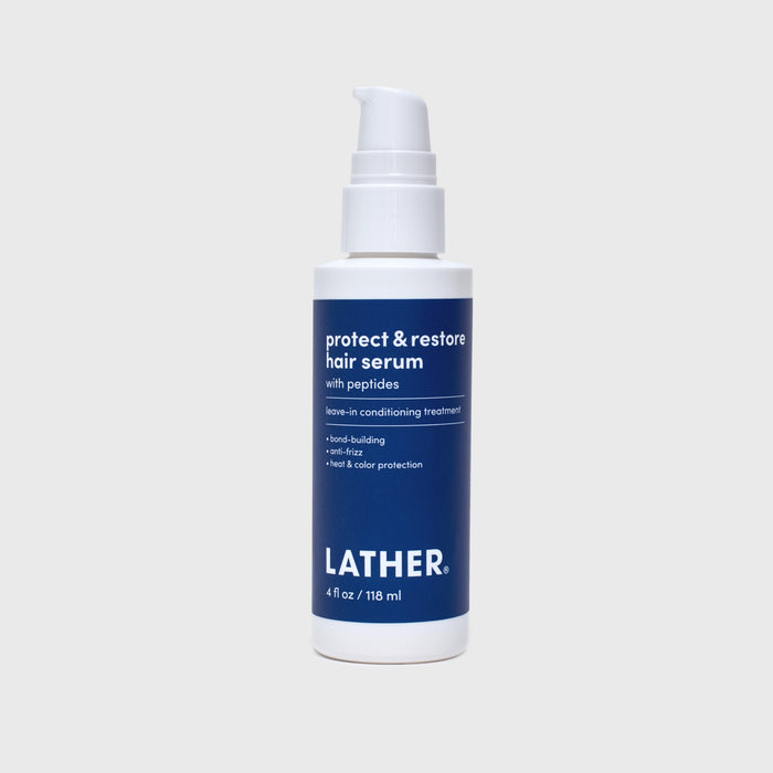 A bottle of Lather Protect & Restore Hair Serum with peptides, featuring a white pump bottle and a navy blue label, set against a light gray background.
