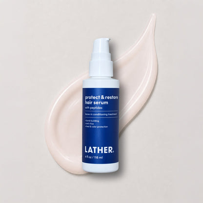 A bottle of Lather Protect & Restore Hair Serum, featuring a white pump bottle with a blue label, set against a beige background with product swatched behind it.