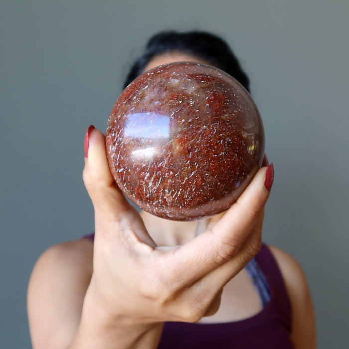 hand holding red hematite quartz sphere