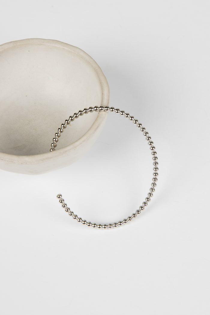 Silver beaded bracelet on a white surface with a neutral background