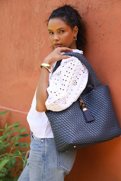 Female model wearing Saskia Denim Blue faux leather Woven Tote over her shoulder with the two shoulder handles