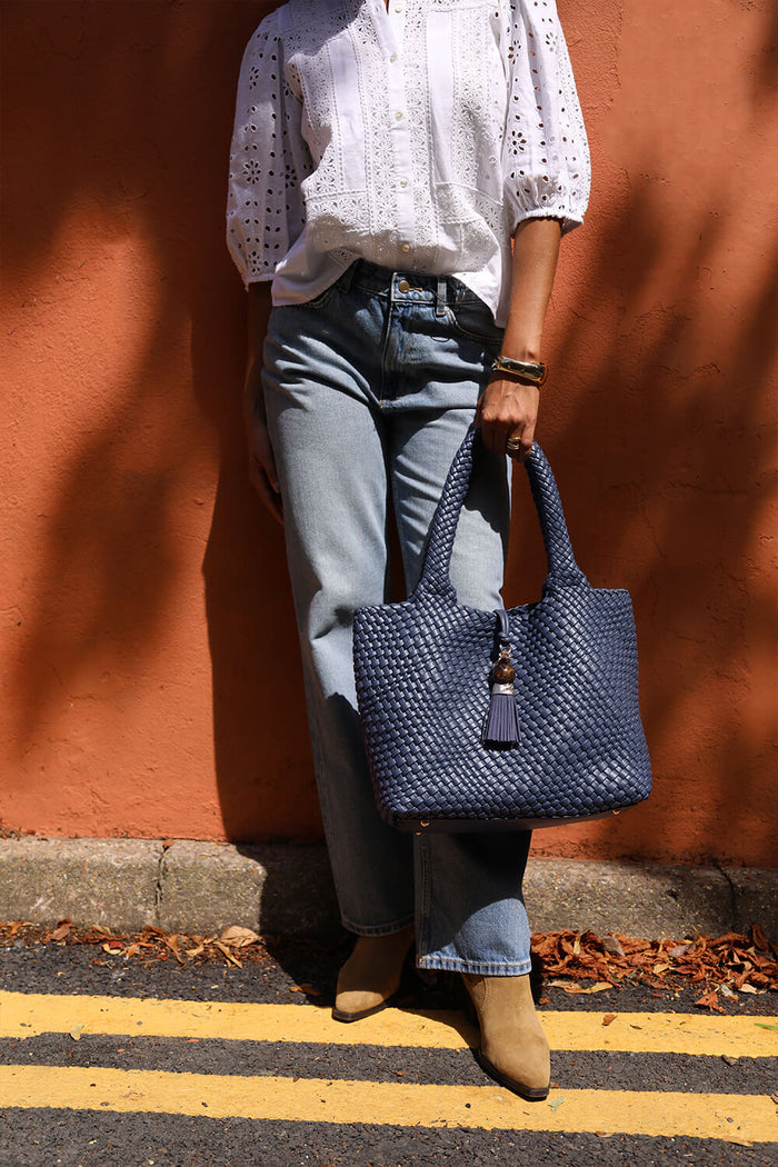 Female model holding Saskia Denim Blue faux leather Woven Tote in her hand using the two top shoulder handles