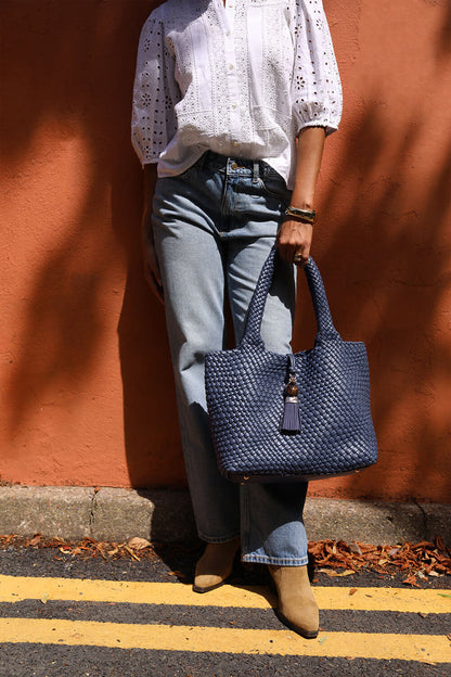 Female model holding Saskia Denim Blue faux leather Woven Tote in her hand using the two top shoulder handles