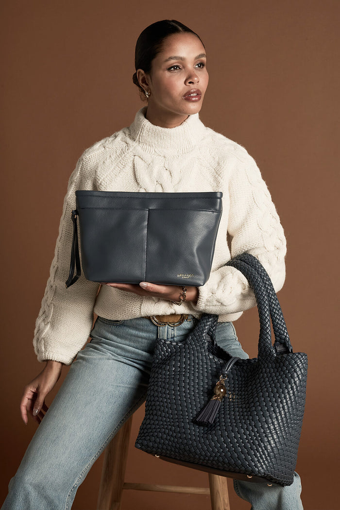 Female model wearing Saskia Denim Blue faux leather Woven Tote over her arm with the two shoulder handles and holding the detachable zipper pouch in her hand