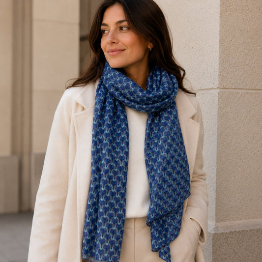 Woman wearing a blue patterned scarf and beige coat against a beige wall.