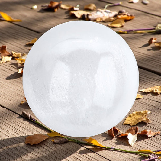 Round white selenite sphere on a wooden surface with leaves