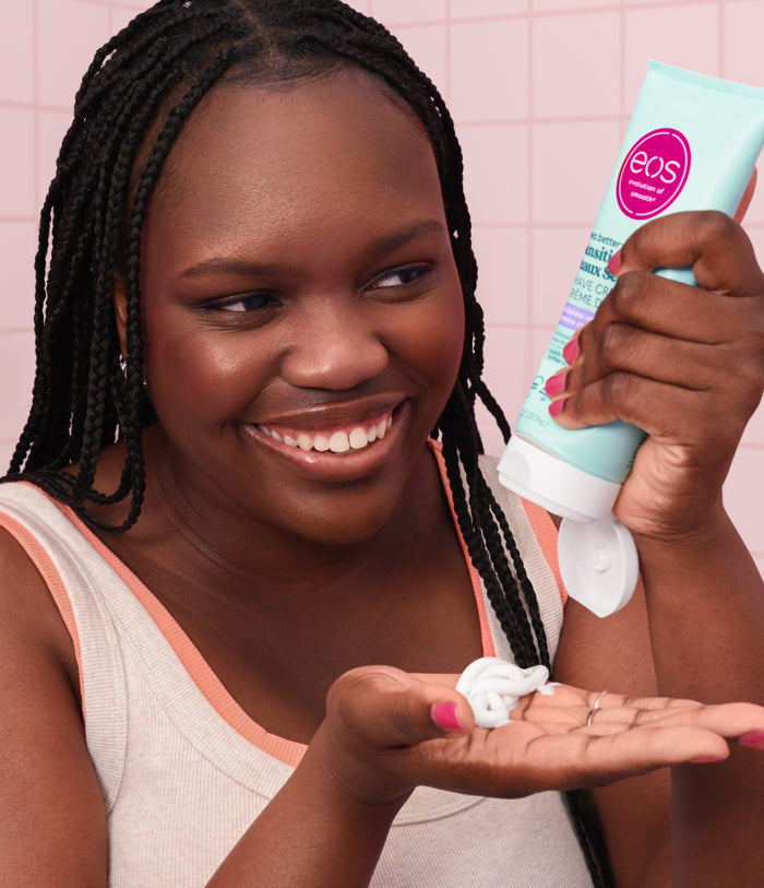 Woman holding a tube of EOS lip balm against a pink background