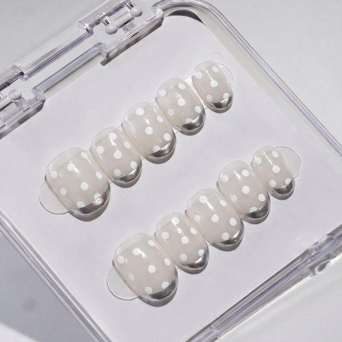 EyeCandys Silver Spotted Press-On Nails feature a light beige base with white polka dots, neatly arranged in two rows inside a clear case for an easy salon-gel manicure at home.