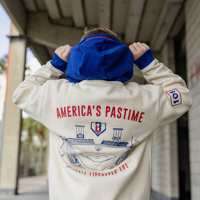 Back view of boy pulling up the royal blue hood of a cream stadium hoodie showing the back graphic and 101 sleeve patch