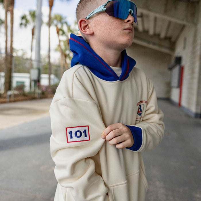 Boy looking up wearing teal shield sunglasses and a cream stadium hoodie with royal blue hood and cuffs