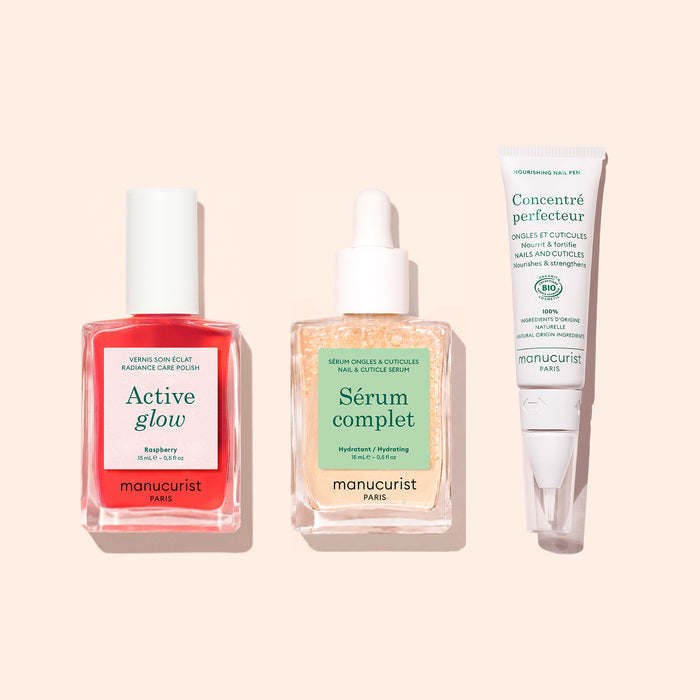 The Basic Routine - Sensitive Nails set from Manucurist features three essential manicure products—a red Active Glow nail polish, a Sérum Complet dropper bottle, and a white Concentré Perfecteur tube—beautifully arranged on a pale pink background to help rescue and moisturize nails.