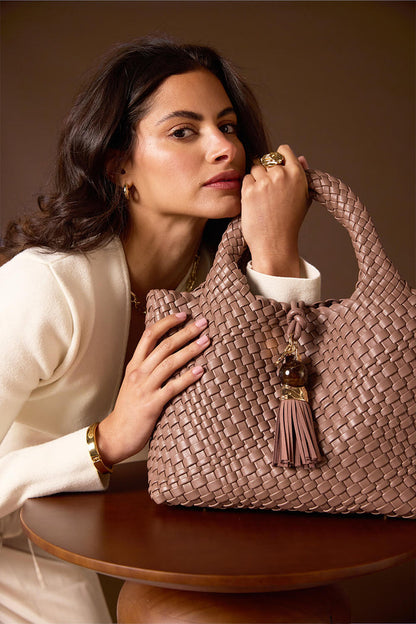 Female model holding Suky Fawn faux leather Woven Crossbody in her hand using the top grab handles