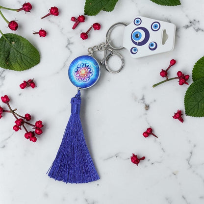 Keychain with blue tassel and decorative pendant on a marble surface with red berries and green leaves.