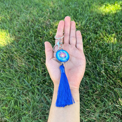 Hand holding a keychain with a blue tassel against a grass background