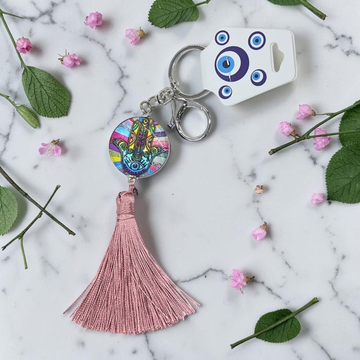 Keychain with tassel and colorful design on a marble surface with flowers and leaves.