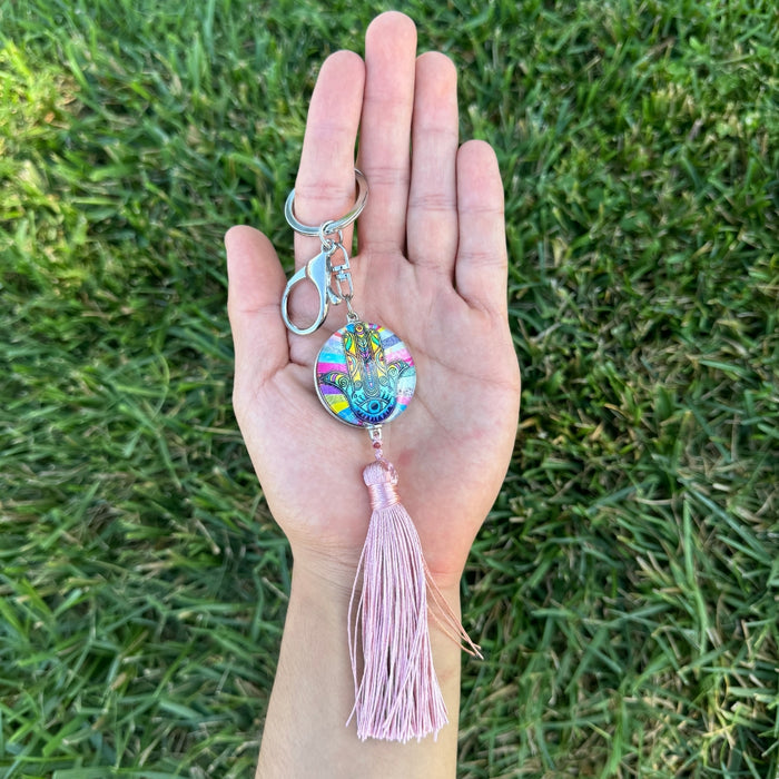 Hand holding a colorful keychain with a tassel against a grass background