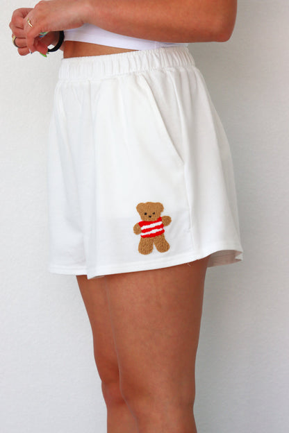 girl wearing white lounge shorts with a teddy bear patch