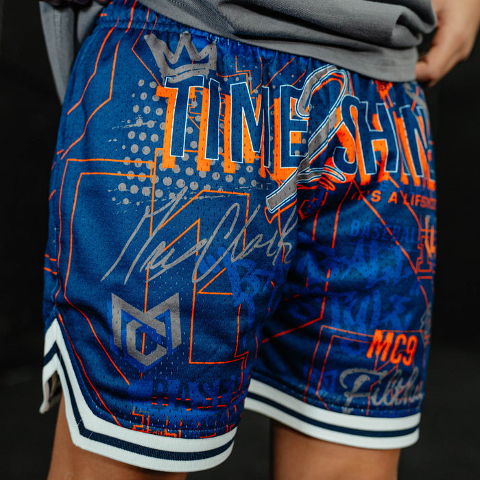 Blue athletic shorts with orange and white text and graphics on a dark background