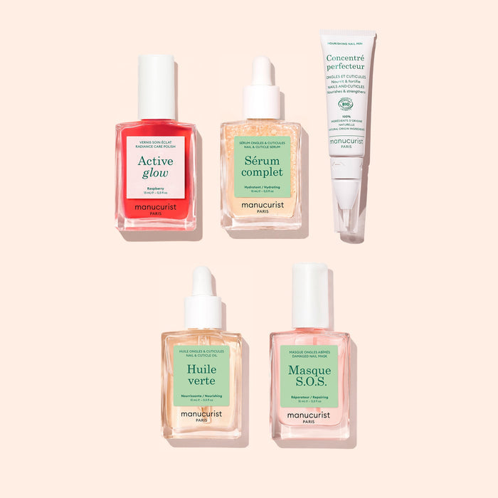 Five skincare products from Manucurist, including serums, oils, and a cream from the Ultimate Routine - Sensitive Nails collection, are arranged on a light pink background. Among them is a nourishing cuticle serum formulated to strengthen nails and enhance your nail care routine. Each product features a pastel-colored label highlighting its name and specific purpose.