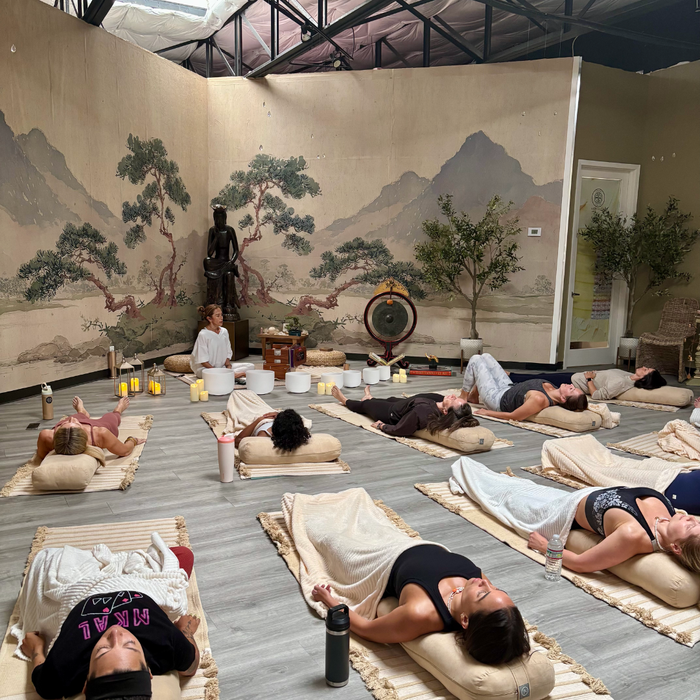 BuDhaGirl yin yoga and immersive sound bath session with participants resting on mats in a tranquil studio surrounded by mountain murals and singing bowls