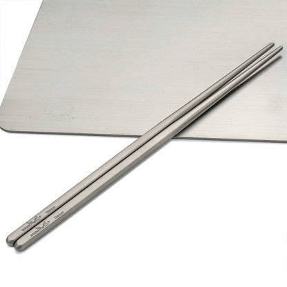 Two Winnerwell® square titanium chopsticks placed side by side on a flat surface, emphasizing their uniform square shape and metallic finish.