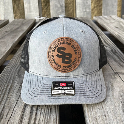 Youth-sized snapback cap with heather grey and black colors, featuring a leather patch logo on the front.