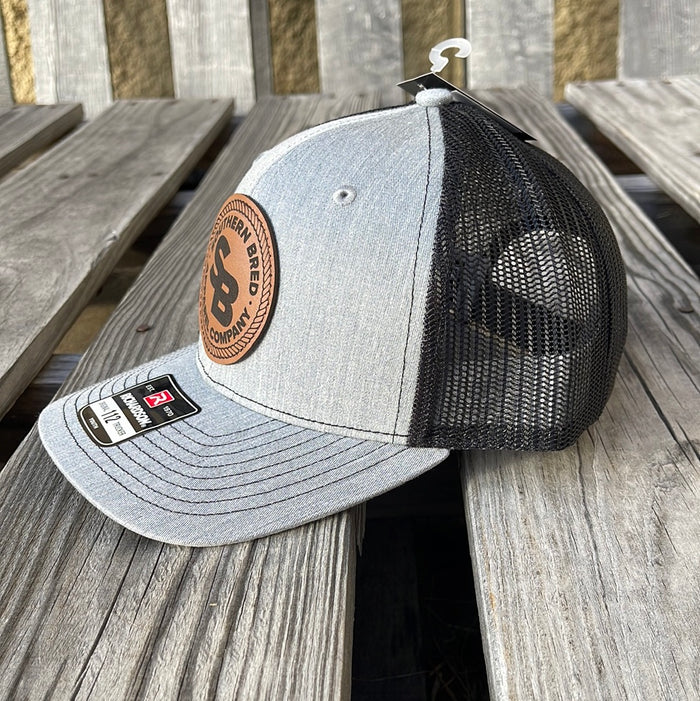Side view of a youth-sized snapback cap with heather grey and black colors, featuring a leather patch logo on the front.