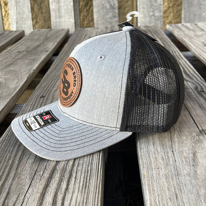 Side view of a youth-sized snapback cap with heather grey and black colors, featuring a leather patch logo on the front.